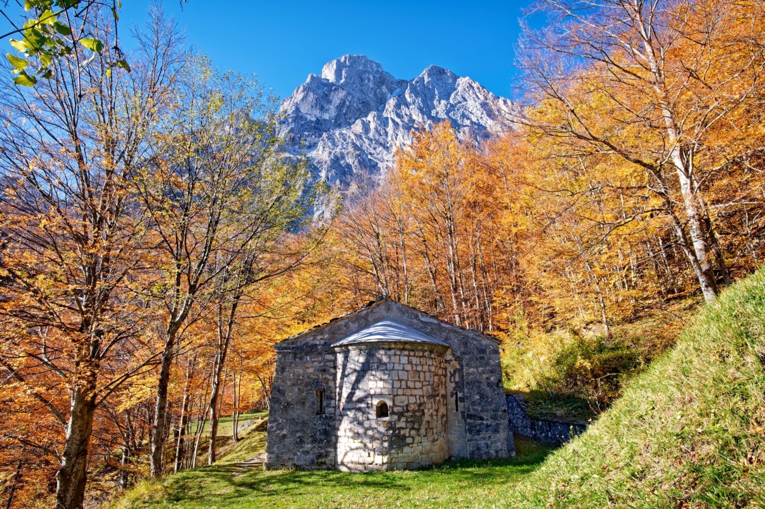 Cappella in pietra in un bosco d'autunno ai piedi delle montagne innevate