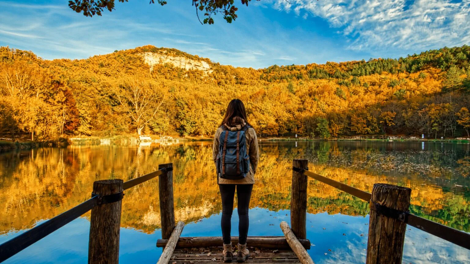 Escursionista su un pontile di legno davanti a un lago in autunno